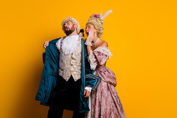 Fototapeta premium Royal couple in historical costumes sharing laughter against vibrant yellow backdrop
