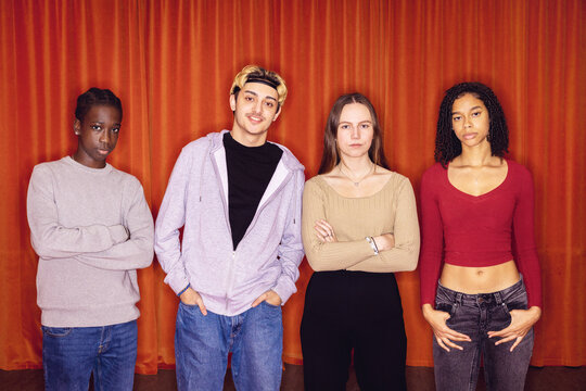 Portrait of multiracial male and female friends standing in front of red curtain