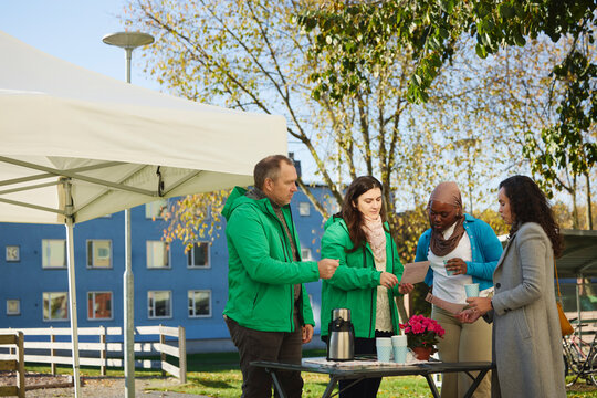 Female volunteer showing pamphlet to neighbors while standing at table in park