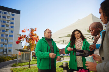 Male and female charity volunteers giving flyers to woman in park under clear sky