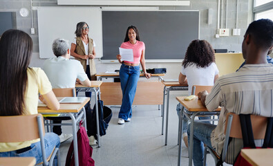 African American female student doing presentation reading essay to classmates and teacher at High...