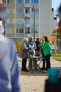 Male and female volunteers discussing about charity work with multiracial neighbors at public park