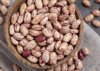 Wooden bowl full of dried pinto beans on napkin top view. Traditional Latin American legumes