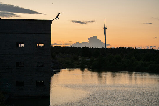 Unrecognizable person jumping from top of abandoned building in water at sunset
