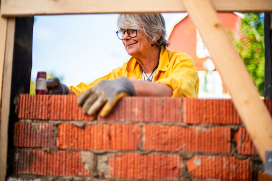 Smiling mature woman layering bricks during house renovation