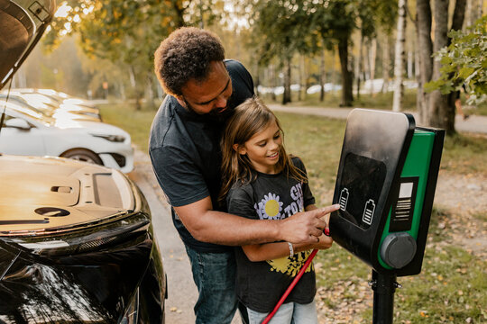 Father assisting daughter in using electrical charging outlet at street