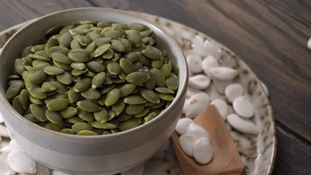 Small bowl filled with green pumpkin seeds placed on plate surrounded by white pumpkin seeds.