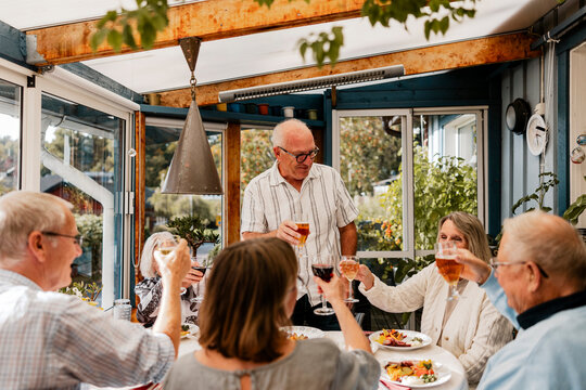Smiling senior man doing celebratory toast with family friends at patio of house - Powered by Adobe