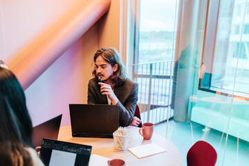 High angle view of long haired businessman sitting with laptop in meeting room at office