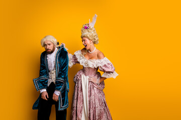 Fototapeta premium Young couple in glamorous vintage costumes posing against a vibrant yellow backdrop