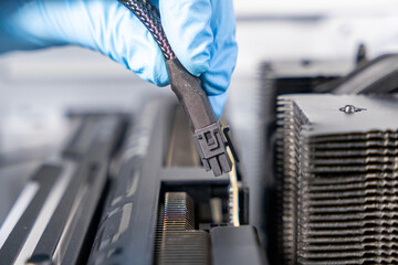 Technician in blue gloves holding 12VHPWR PCIe power cable above graphics card slot during PC...
