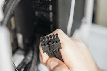 Close-up of technician holding black 8-pin power connector for motherboard or GPU during computer...