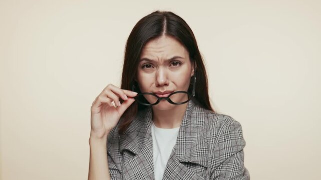 A confident young woman in a stylish suit removes her glasses with an arrogant expression, scrutinizing the situation.