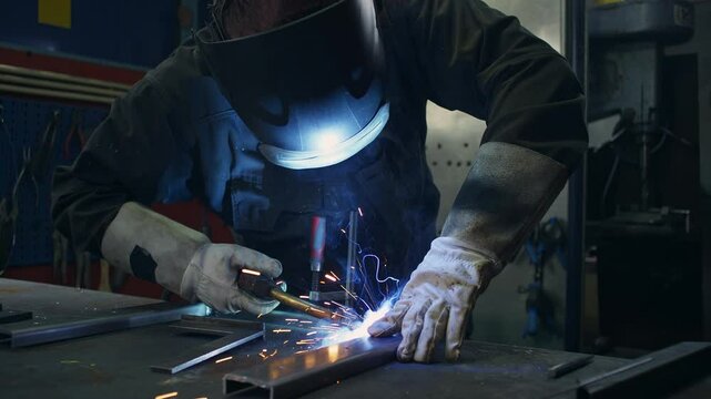 Skilled welder worker with experience in metal fabrication, using MIG welding techniques to create sparks and shape metal components, close up shot.
