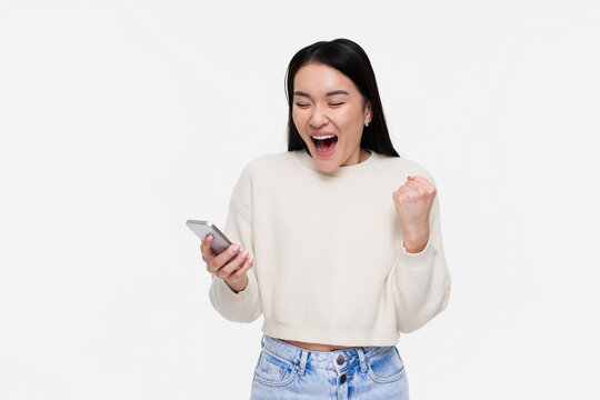 Excited crazy gen z Asian young woman girl winner with smartphone happy shopper customer female student screaming yes using mobile cell phone celebrating online prize win on white background.