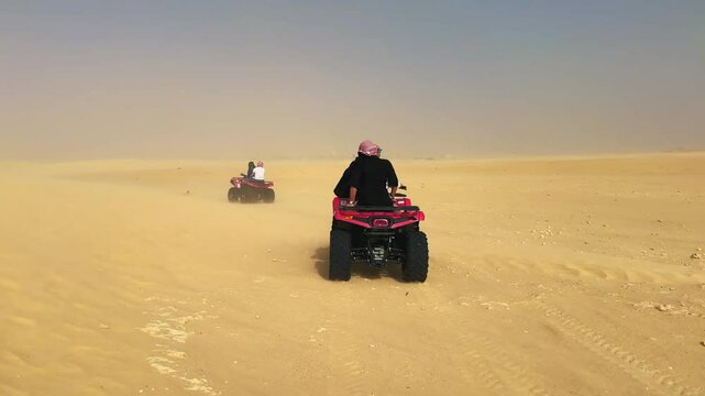 People ride on quad bikes traverse the dusty, sunlit expanse of the Sahara desert, creating an adventurous and dynamic scene