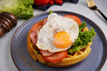 Fresh waffles with fried eggs, lettuce, tomatoes and served for breakfast on a flat table.