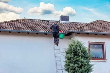 worker on the roof. man on ladder cleaning house gutter from leaves and dirt. 