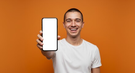 Smiling young man holding smartphone with blank screen on orange background