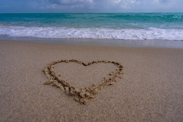 Heart drawn in sand. Waves forming a heart shape sign. Love on beach. Romantic summer. Heart made of sand. Love and ocean waves.