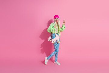Young stylish blonde woman posing casually with roller skates against pink background showcasing...