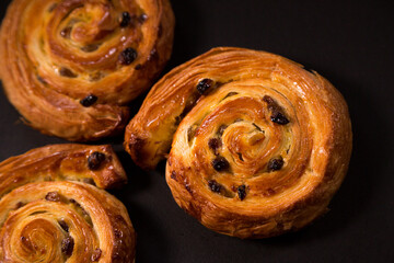Puff pastry snail with maple syrup and raisins on a black background, top view