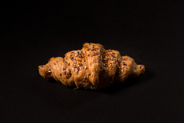 Flaky puff pastry croissant with grains and seeds on a black background, top view