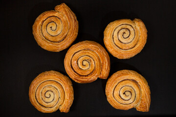 Puff pastry snail with maple syrup and cinnamon on a black background, top view