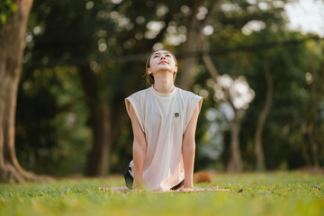 Young Asian woman practicing yoga in a quiet park, gracefully in a relaxed pose, relaxing and...