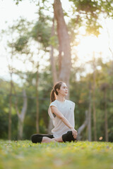 Young Asian woman practicing yoga in a quiet park, gracefully in a relaxed pose, relaxing and...