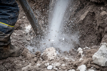 Fototapeta premium Damaged industrial pipeline leaks water during excavation work at construction site