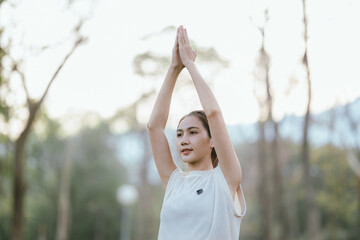 Young Asian woman practicing yoga in a quiet park, gracefully in a relaxed pose, relaxing and...
