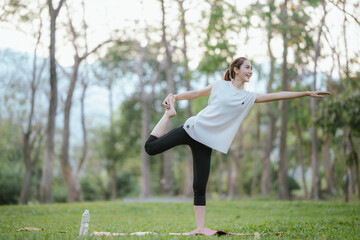 Young Asian woman practicing yoga in a quiet park, gracefully in a relaxed pose, relaxing and...
