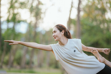 Young Asian woman practicing yoga in a quiet park, gracefully in a relaxed pose, relaxing and...
