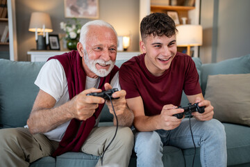 Grandfather and grandson playing videogames on sofa at home © Migma_Agency