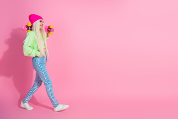 Stylish young woman in casual trendy outfit holding skateboard against vibrant pink background, blending charm