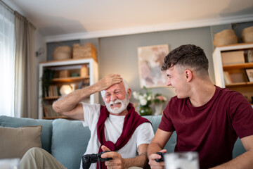 Fototapeta premium Grandfather and grandson playing video games at home, experiencing different emotions