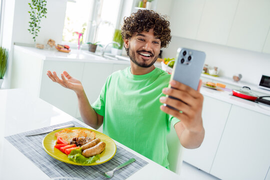 Young man enjoying a meal while capturing a moment on his smartphone in a bright, modern kitchen, reflecting joy and culinary creativity