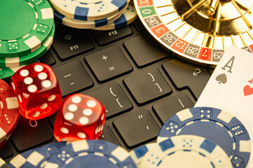 High-resolution composite image of casino chips, closed laptop, moving roulette wheels, playing cards ace of spades, ace of hearts, and designed for marketing in gambling or gaming services