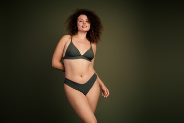 Obraz premium Confident young woman embracing natural beauty in stylish underwear, modeling on khaki background