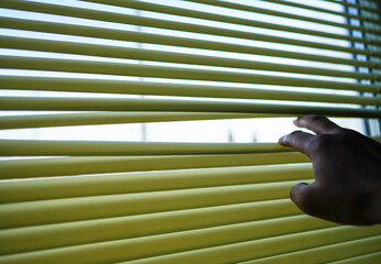 Look through blinds. Man's hand lifts blinds to secretly look through window. Close up hand standing by bedroom window, opening curtains. Looking through window blinds, sun light coming inside of room