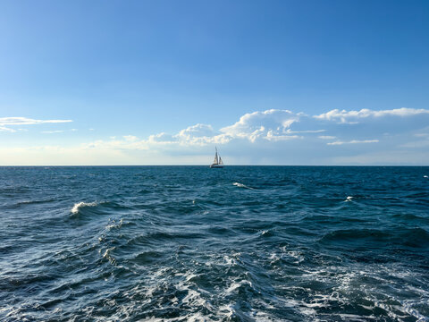 sailboat on the open sea under a blue sky with scattered clouds, calm waves and natural light. deep blue sea