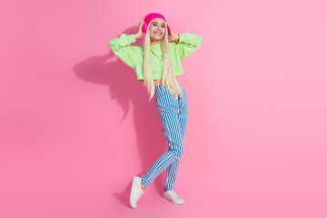 Charming young woman in colorful casual outfit posing on pink background showcasing modern fashion styles with a beanie hat