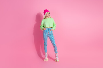 Trendy young woman posing in colorful casual attire with roller skates on vibrant pink backdrop,...