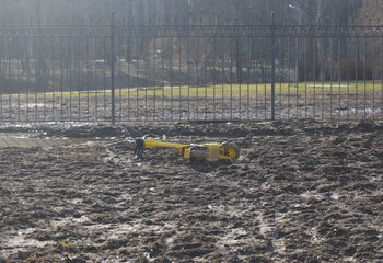 A yellow electric scooter is lying in the mud near a lattice fence