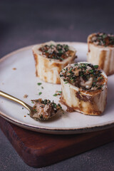 Homemade Roasted Beef Bone Marrow with spoon and croutons on a plate, wooden board, grey background. Side view. Close up.
