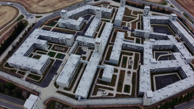 High angle view revealing sprawling prison complex with multiple interconnected buildings, watchtowers, concrete courtyards, and surrounding perimeter roads