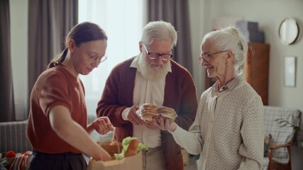 Young woman unpacking fresh groceries from paper bag for grateful senior grandparents at home, elderly man checking shopping list on smartphone - Powered by Adobe