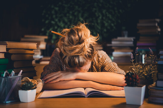 Young student overwhelmed with studies resting head on a book in a cozy home environment