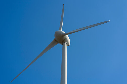 A lone wind turbine against a blue sky and white clouds. Green energy concept